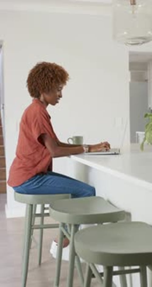 Vertical video: African American woman placing hands on keys typing for work at kitchen on laptop