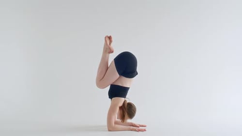 Mujer joven haciendo pose de escorpión mientras practica yoga en un estudio minimalista