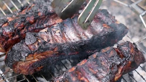 Kochen von eingelegten Schweinerippchen auf einem Grillrost auf Lagerfeuerkohle