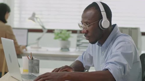 Black Businessman In Headphones Working on Laptop in Office