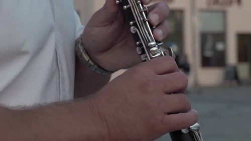 Musician in a white shirt plays the clarinet. Pan up. Close up. Street performance.