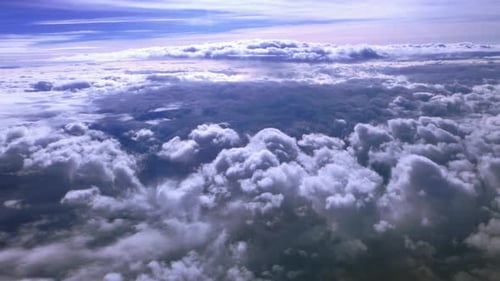 A high altitude aerial view above the clouds on a sunny day from the cabin of a passenger plane.
