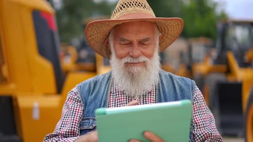 Senior Man Uses Tablet Near Tractors