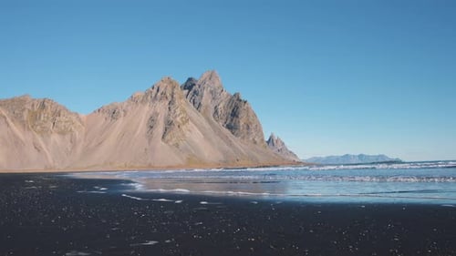Waves washing black sand beach below sharp Vestrahorn mountain peak.