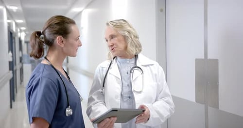 Caucasian female doctors in discussion using tablet in hospital corridor, slow motion
