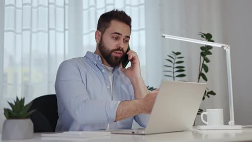 Competent Male Freelancer Having Phone Call While Sitting at Home Office