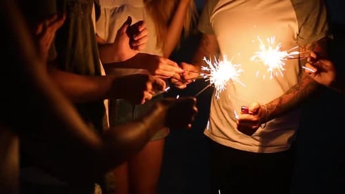 Amigos em pé ao redor de uma fogueira durante uma festa noturna à beira-mar para acender faíscas de Bengala