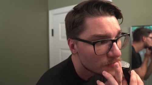 Young Man Trims Beard in Bathroom Mirror