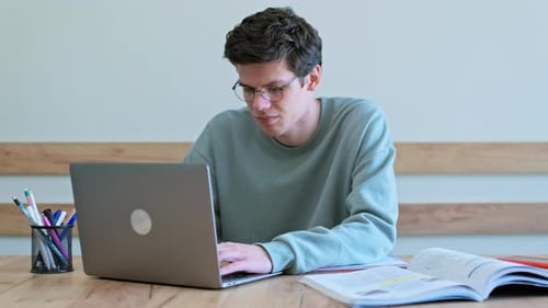 Young Guy College Student Sitting at Desk in Classroom Typing on Laptop
