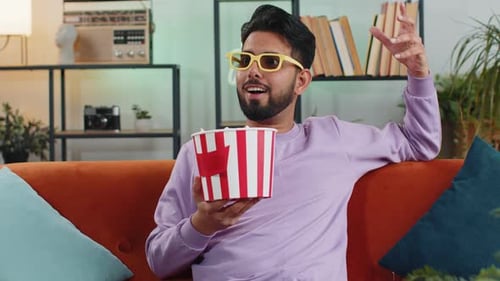 Man Eats Popcorn on Couch Wearing Glasses