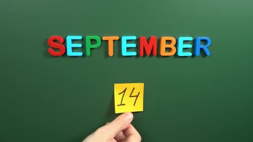 Hand sticking a sticker 14 September calendar day on school board. 14 date of September. Fourteenth