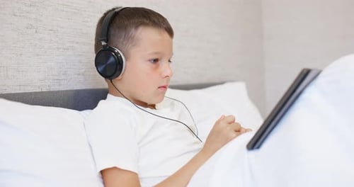 Boy in Bed Using Tablet with Headphones