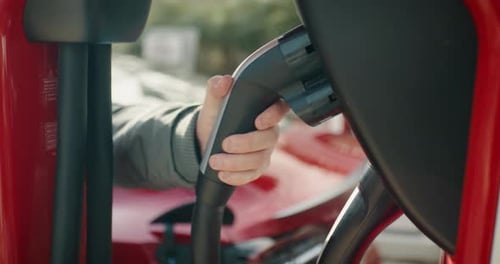 Close up of pulling out the charging cable of the charging station and plugging it into the car