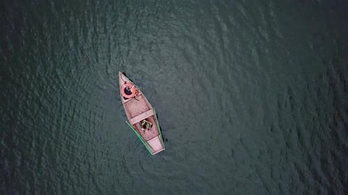 Um barco de pesca sereno flutuando suavemente em águas calmas, refletindo a beleza da natureza ao seu redor Stock Clip
