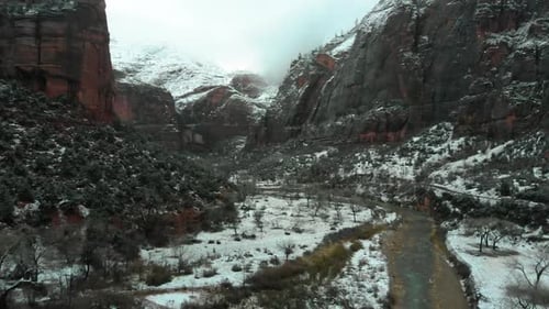 Machen Sie eine Aufnahme des schneebedeckten Bodens zwischen den Bergen mit einem fließenden Fluss darunter.