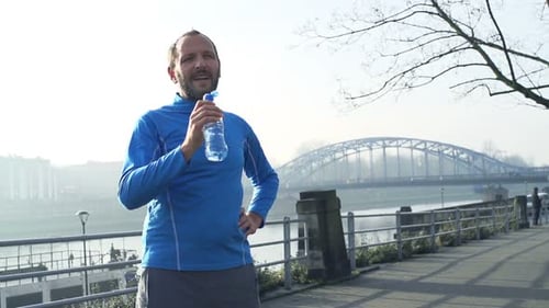 Young Male Jogger Resting and Drinking Water in City, Super