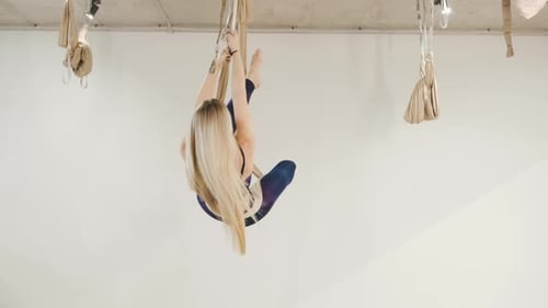 Portrait of Young Blonde Fit Woman Doing Aerial Yoga Exercise on Hammock in Yoga Studio