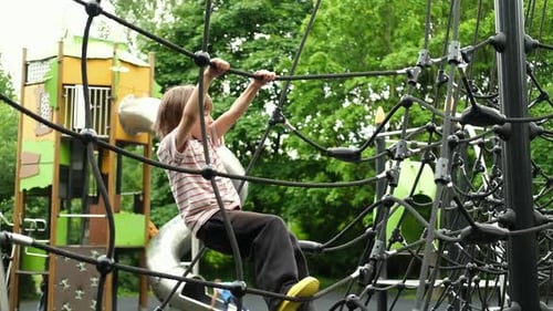 A Child Boy is Climbing Up an Alpine Grid in a Park on a Playground on a Hot Summer Day Kids