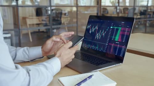 Man analyzing stock market data using phone and laptop