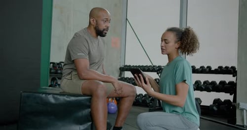 Fitness Instructor Looking at results on Digital tablet with Client in Gym