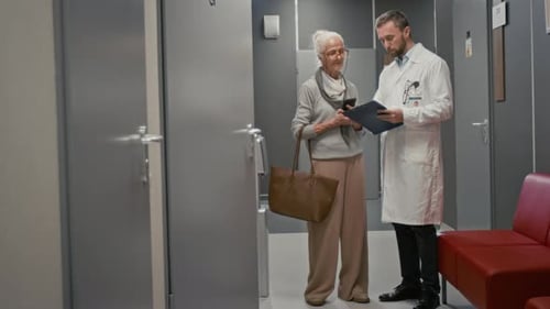 Doctor Talking to Senior Patient Standing in Hall
