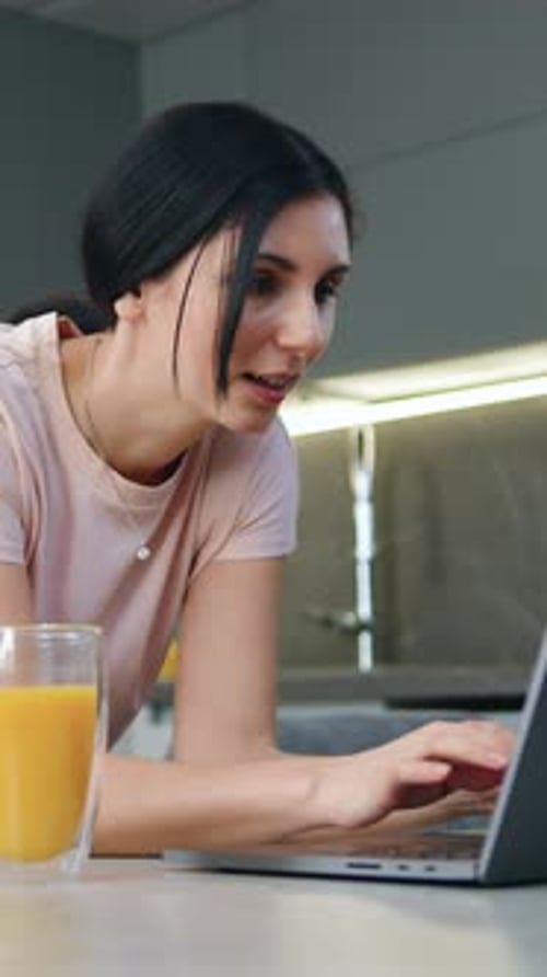 Woman Using Laptop in Kitchen With Orange Juice