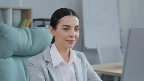 Smiling Woman Sits in Office, Looks at Camera