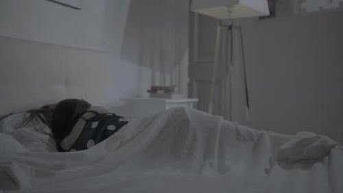 Mujer durmiendo tranquilamente en su cama en el dormitorio donde se enciende su lámpara de noche sobre un soporte plateado