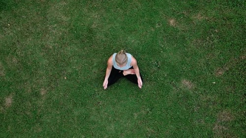 Sporting Woman Doing Yoga Exercises and Breath Meditation Sitting on Green Grass