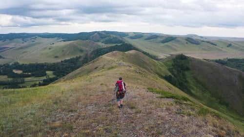 Male Tourist with a Large Backpack Walks Along a Hilly Ridge Enjoying Beautiful Views
