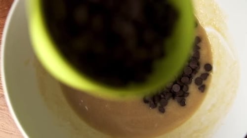 Makro von oben nach unten, beim Gießen von Schokoladenstückchen in eine Schüssel mit Zutaten