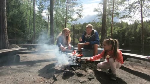 A Couple with a Child Grilling in the Forest on the Shore of the Lake