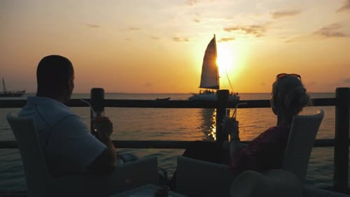Young couple enjoying their cocktails in ocean chillout bar watching magical summer sunset with yach