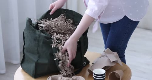 Reciclado. Mujer poniendo papel usado en una bolsa en una mesa de madera en el interior, de cerca. Ampliación de la cámara