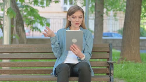 Video Chat via Tablet by Woman Sitting on Bench in Park