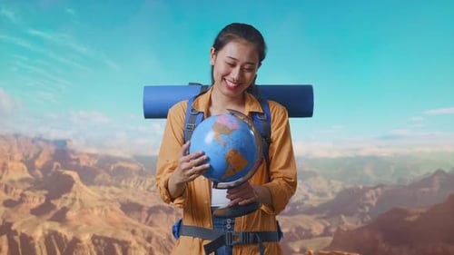 Asian Female Hiker Holding World Globe In Her Hands And Smiling At The Top of Mountain