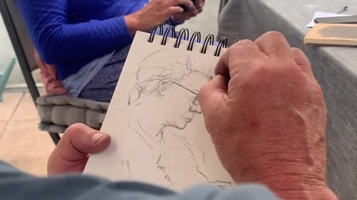 Male Artist Sketches Woman's Face on Notepad with Pencil in Garden
