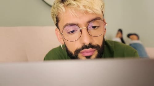 Close-up, young blond man with a beard uses a laptop while lying on the sofa in a cozy living room