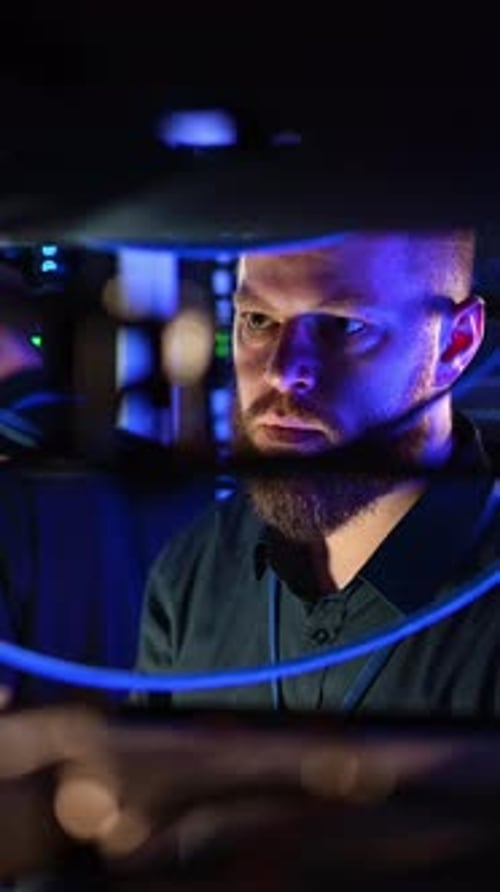 Focused Man Working in Server Room Under Blue Lights