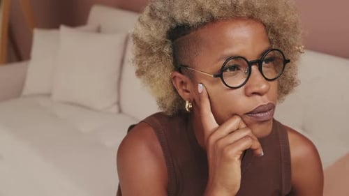 Close up, thoughtful young woman sitting on sofa in apartment, with pensive face looking away