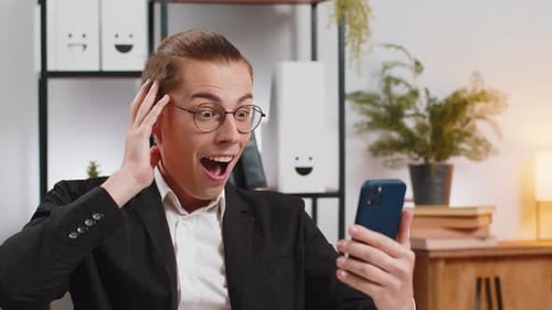 Young Man Reacts to Exciting News on Smartphone