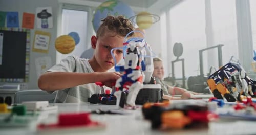 Grundschüler sitzt am Schreibtisch und untersucht Modell eines innovativen Roboterarms