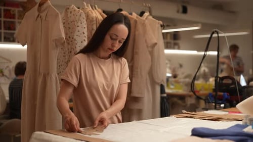 Focused Female Dressmaker Arranging Cardboard Sewing Patterns on Table in Professional Atelier