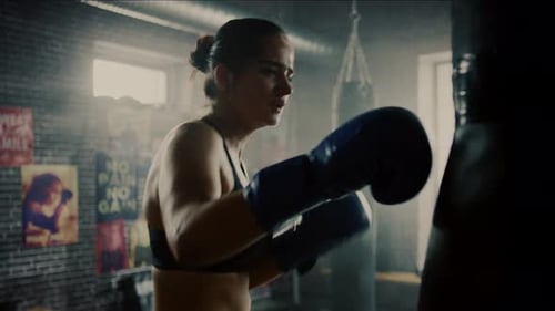 Fit Athletic Woman Kickboxer Punches and Hits the Punching Bag During a Workout in a Loft Gym with