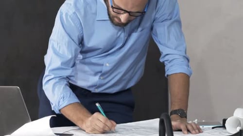 Man Reviews Blueprints at Desk in Office