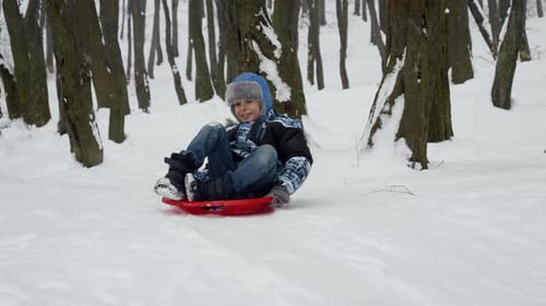Zeitlupenaufnahmen eines glücklichen und lächelnden Jungen, der freudig einen verschneiten Hügel hinunterrutscht