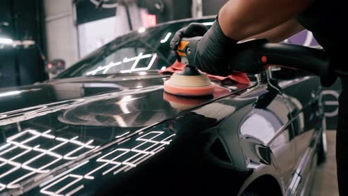 Close-up of a car wash worker using a polishing machine to polish the hood of black luxury car
