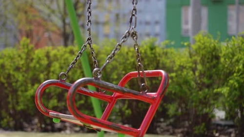 Closeup Empty Metal Swing Seats Swinging on Metal Chains on an Outdoor Playground on a Sunny Spring