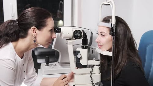 Attentive optometrist examining beautiful female patient with slit lamp in ophthalmology clinic. Opt