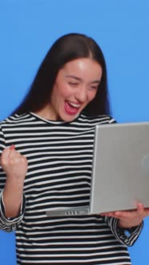 Excited young woman using laptop on blue background